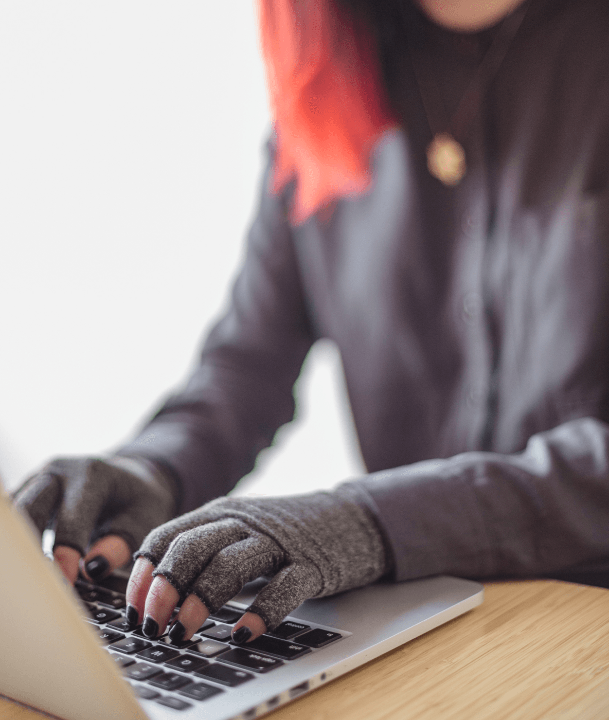 Una persona asiatica disabile genderfluid digita su un computer portatile mentre indossa guanti a compressione. Le mani e la tastiera sono il punto focale.